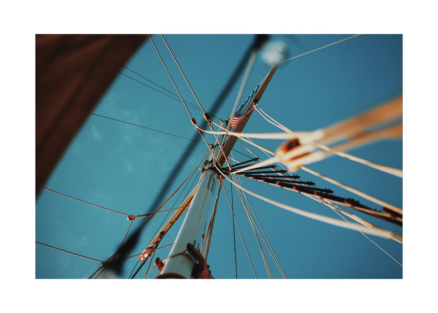 A low-angle view shows the mast and rigging of a sailboat against a clear blue sky.