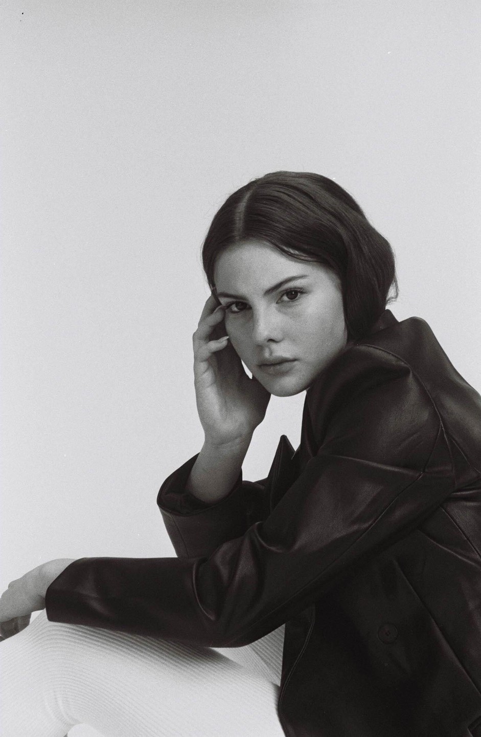 A woman in a leather jacket poses with her hand on her head.