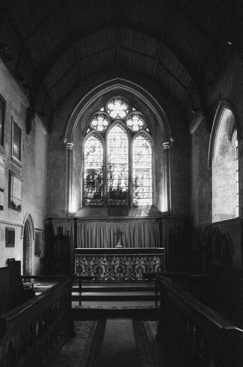 A black and white photograph shows the interior of a church with a large stained glass window at the far end.