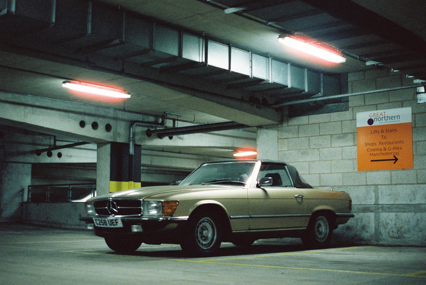 A gold convertible car is parked in an underground garage with neon lights.