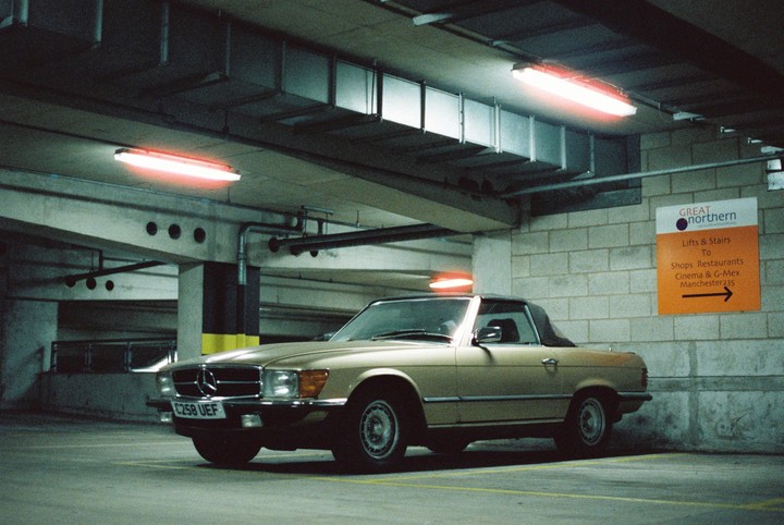 A gold convertible car is parked in an underground garage with neon lights.