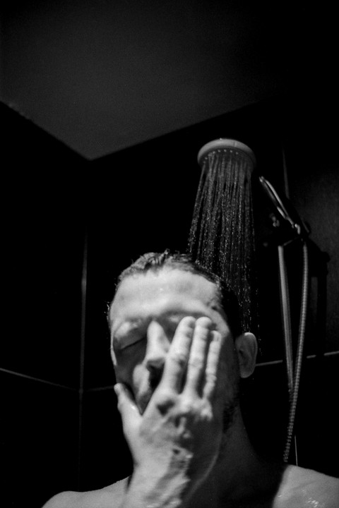A man showers with his hand covering his face.