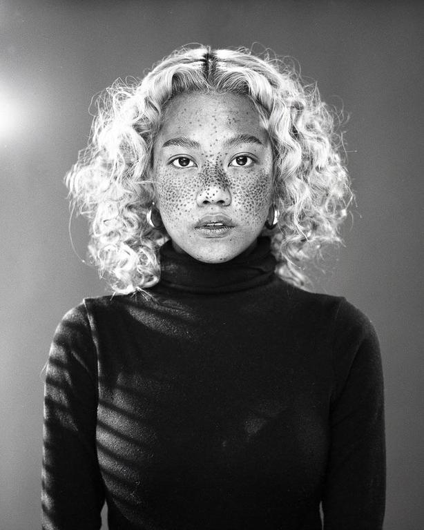 A woman with curly hair and freckles wears a turtleneck and hoop earrings.