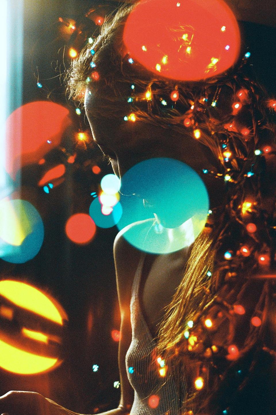 A woman with long hair is illuminated by colorful lights and bokeh.