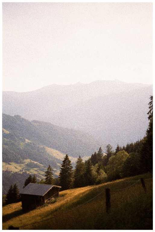 A small wooden cabin sits on a grassy hillside with a forest and hazy mountains in the background.
