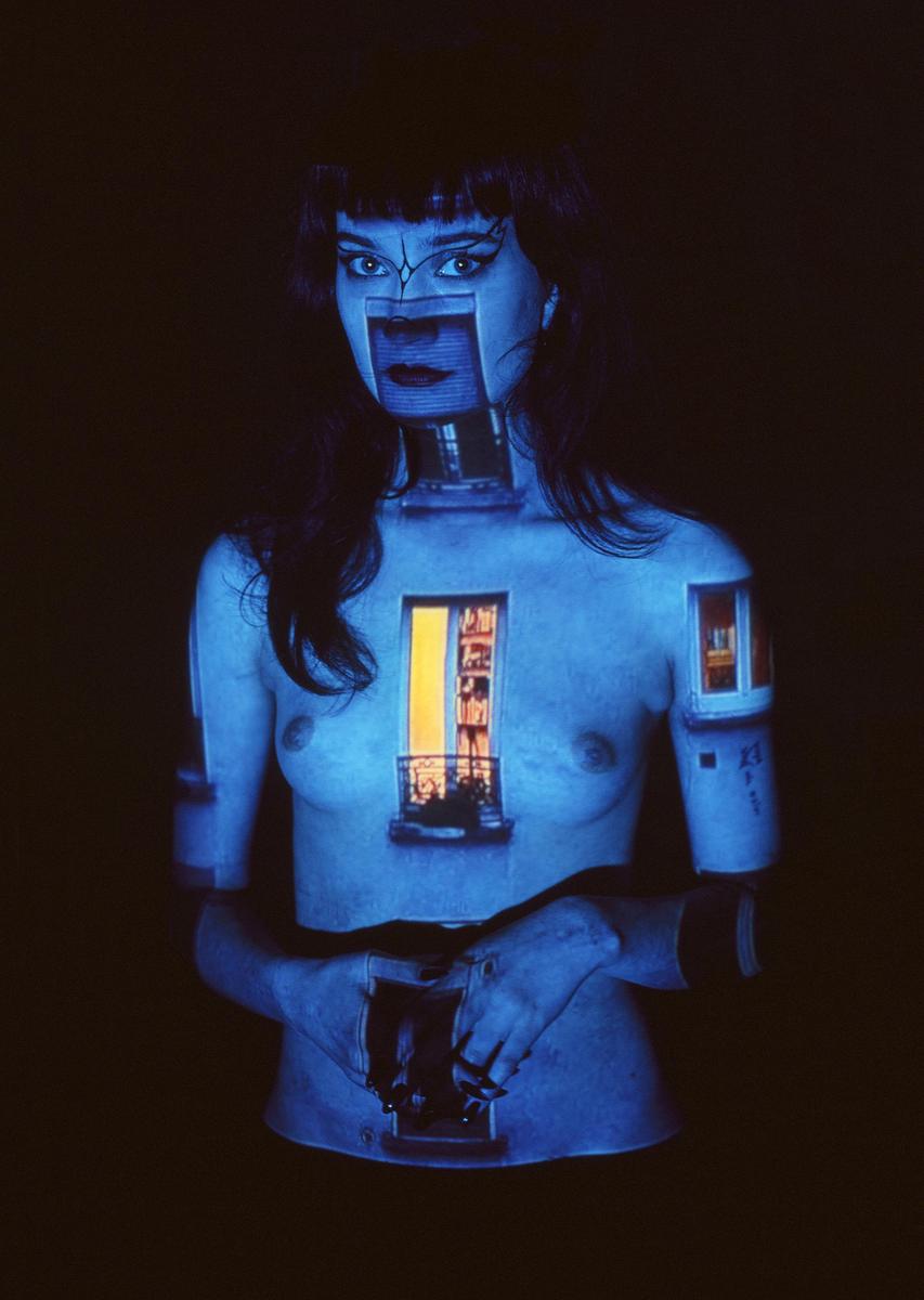 A woman is illuminated by projected images of windows and architectural elements on her body.