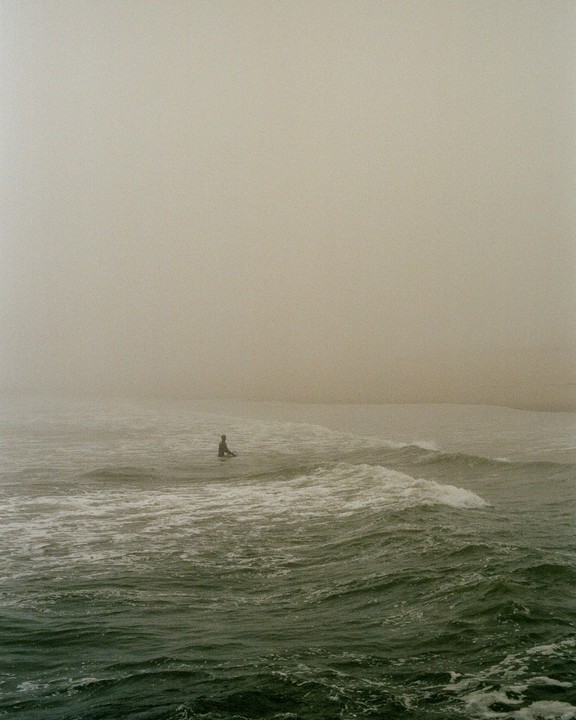 A surfer sits on a surfboard in the ocean on a hazy day.