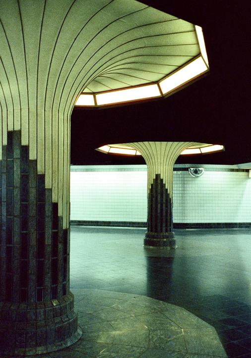 Two decorative columns with illuminated tops stand in a subway station with tiled walls.