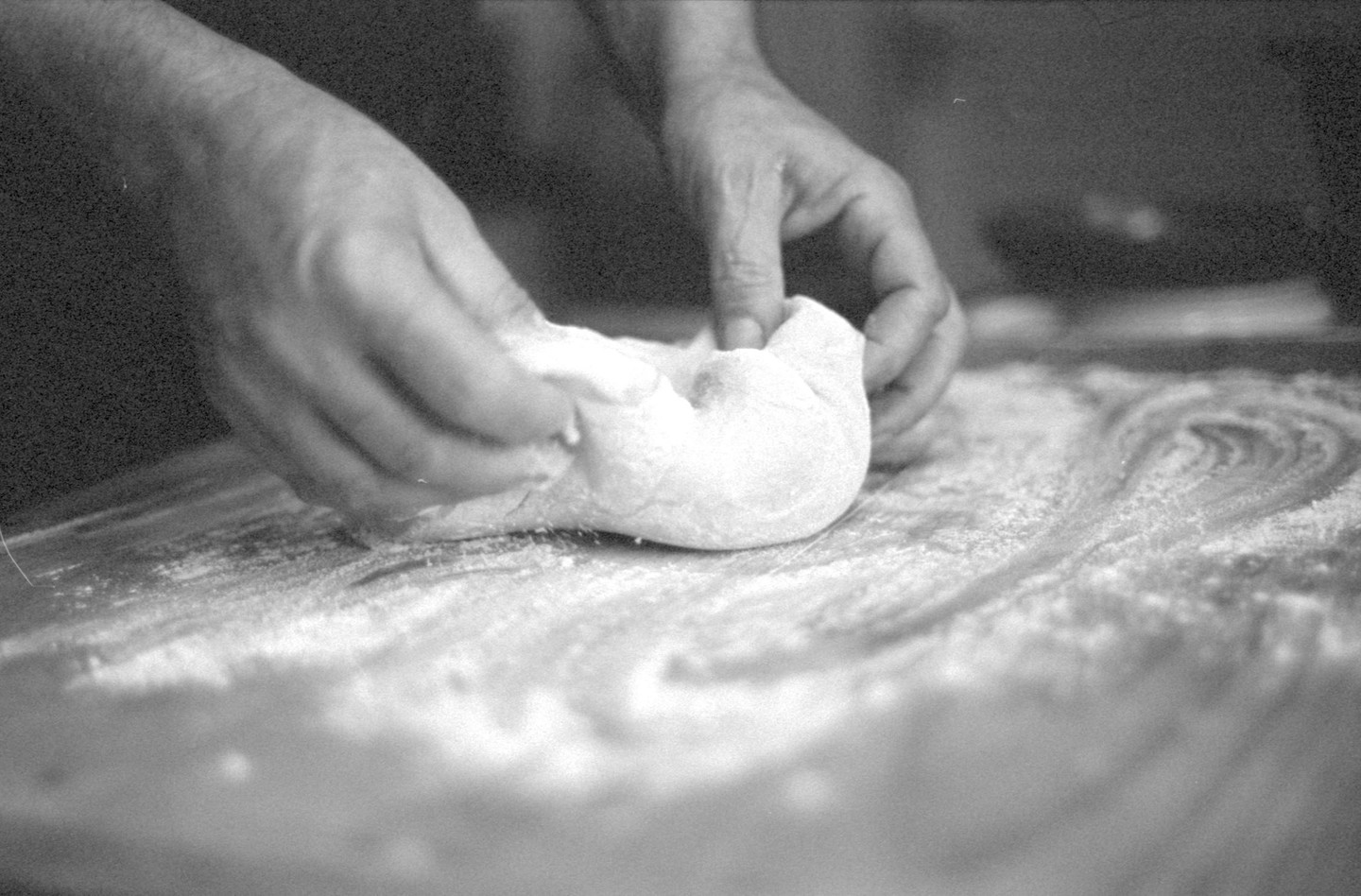 Two hands are kneading dough on a floured surface.