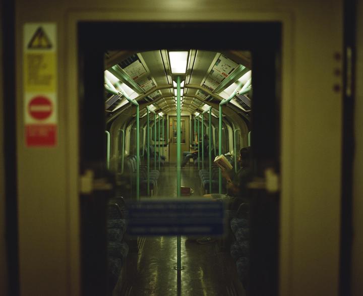 A person reads a book inside a subway car, viewed through an open doorway.