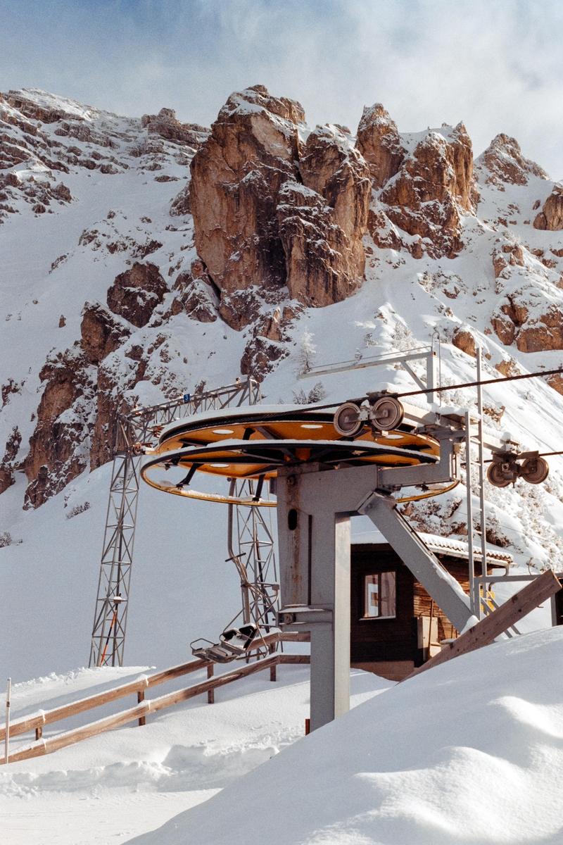 A ski lift with chairs is visible in a snowy mountain landscape with rocky peaks.