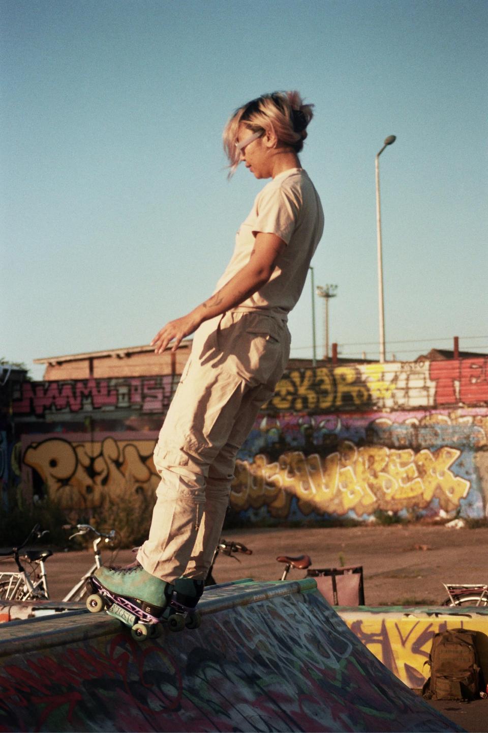 A person on roller skates stands on the edge of a graffiti-covered ramp at a skate park.