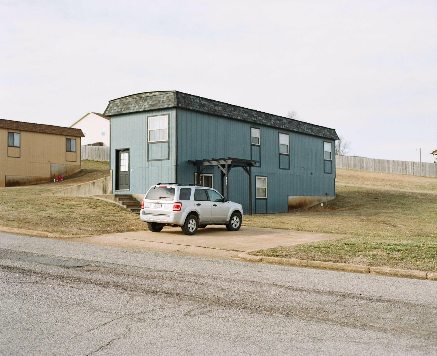 A silver SUV is parked in front of a blue house with a brown house in the background.