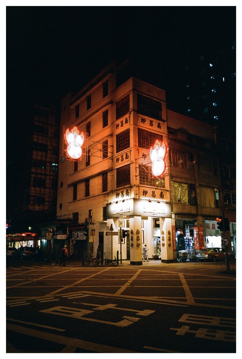 A street corner building with neon signs is illuminated at night.