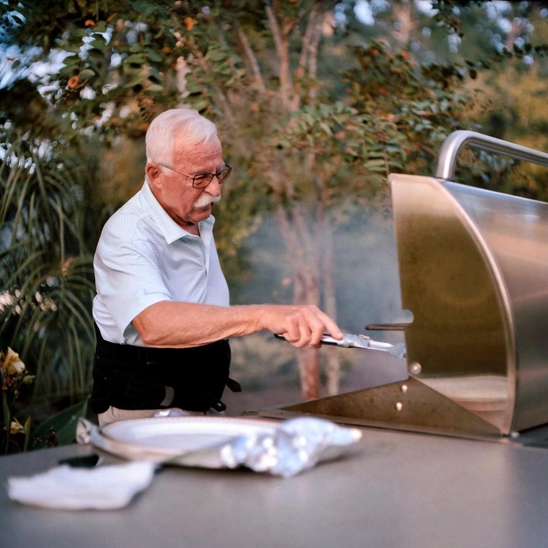 A man with a mustache is grilling outdoors.