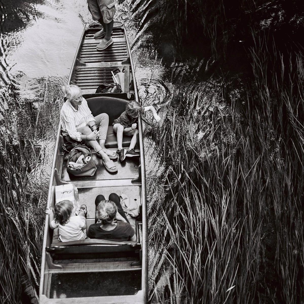 A group of people are punting on a river surrounded by tall grass.