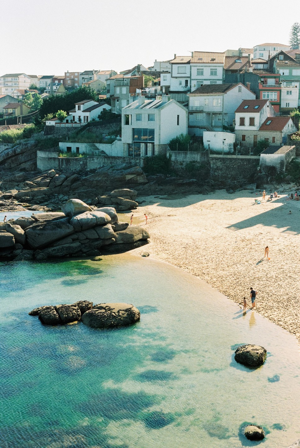 A small beach with clear blue water and a town built into a hillside is visible from above.