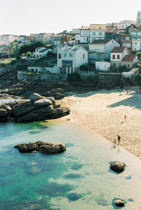 A small beach with clear blue water and a town built into a hillside is visible from above.