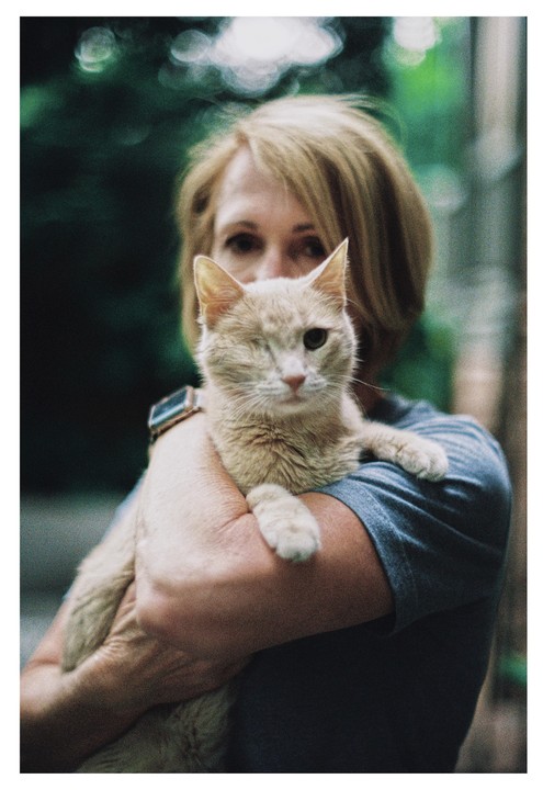 A woman holds a one-eyed cat in her arms.