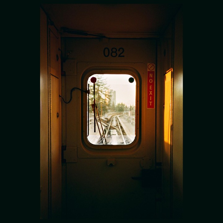 A view from inside a train car shows the tracks ahead through a window, with warm light illuminating the interior.