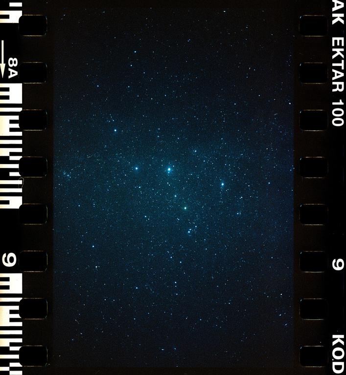 A dark night sky is filled with numerous bright stars, with a cluster of prominent stars visible in the center.