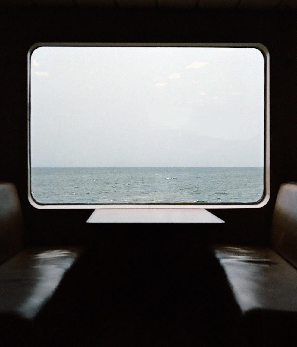 A view of a body of water and a hazy sky is seen through a window from inside a vehicle.