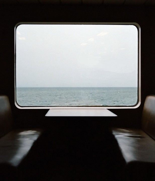 A view of a body of water and a hazy sky is seen through a window from inside a vehicle.