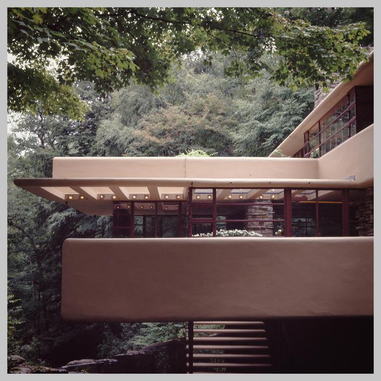 A modern house with multiple levels and balconies is nestled among lush green trees.