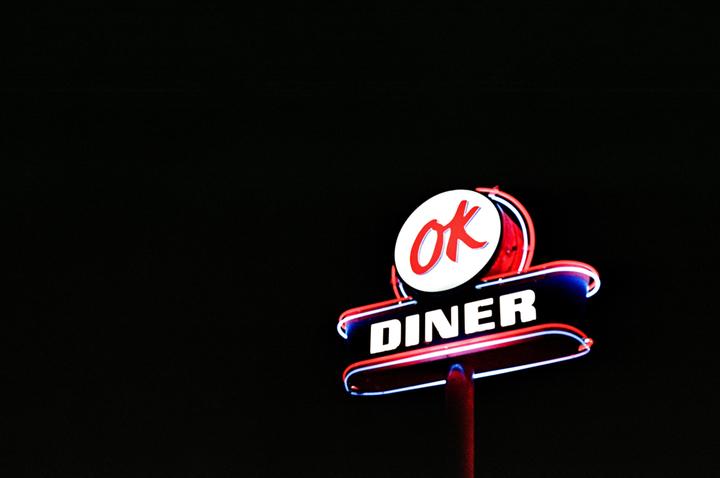 A neon sign for "OK Diner" glows against a dark background.
