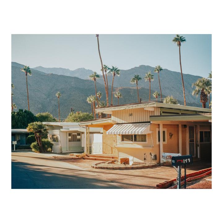 A street with houses and palm trees is visible in front of a mountain range.
