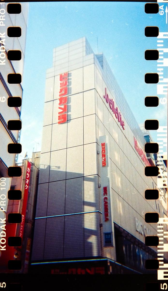 A tall building with red signs is visible from a low angle, with film borders on the left and right.