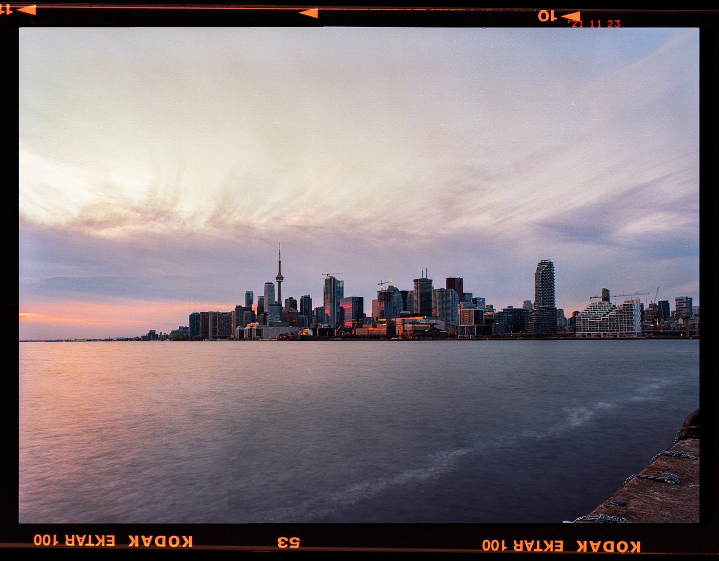 A cityscape with a prominent tower is visible across a body of water under a cloudy sky at dusk.