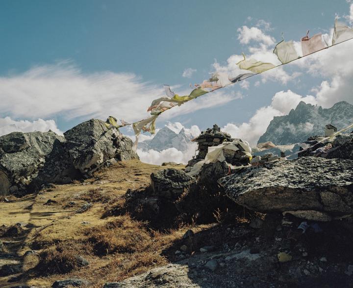 Prayer flags stretch across a rocky, mountainous landscape with clouds in the sky.