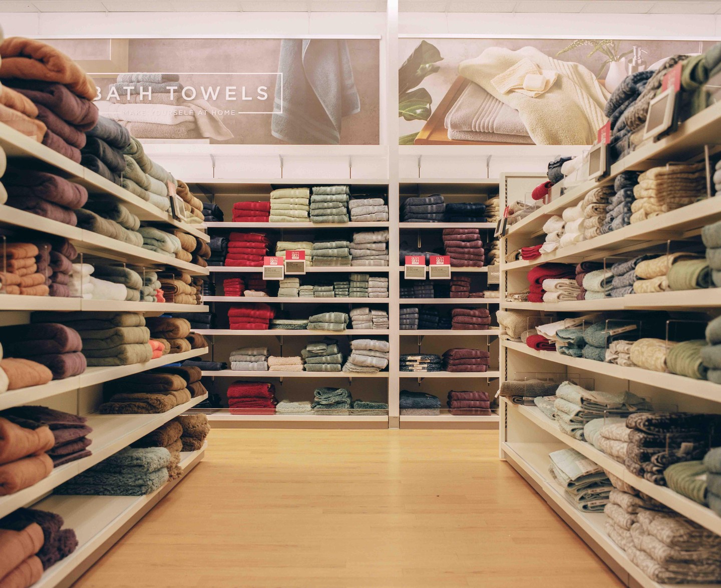 Shelves filled with neatly folded bath towels in various colors are displayed in a store aisle.