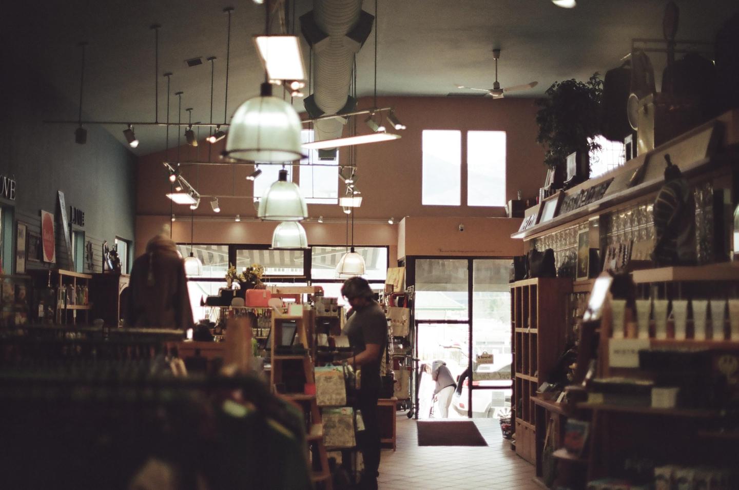 A man stands in a store with various items on shelves and hanging lights from the ceiling.