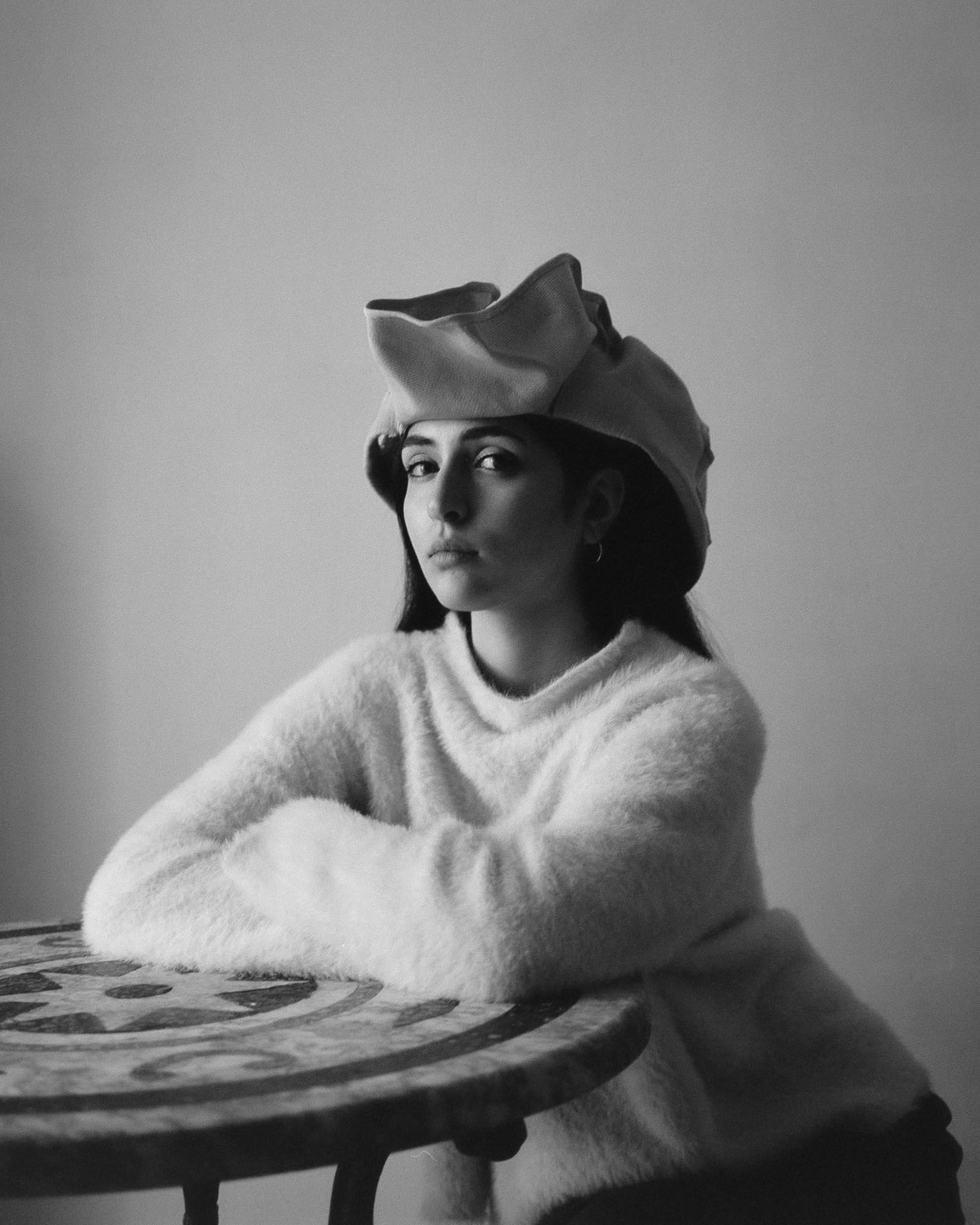 A woman wearing a hat and a fluffy sweater sits at a table.