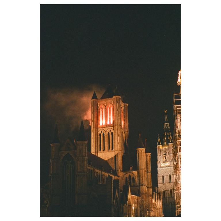 A tall, illuminated church tower stands against a dark night sky, with another building partially visible to its right.