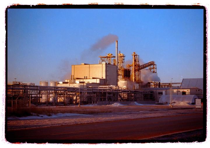 A large industrial complex with smoke rising from smokestacks is visible under a clear sky.