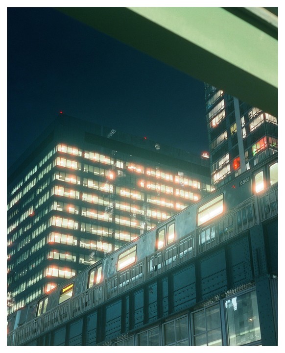 A train passes by illuminated buildings at night in Long Island City.
