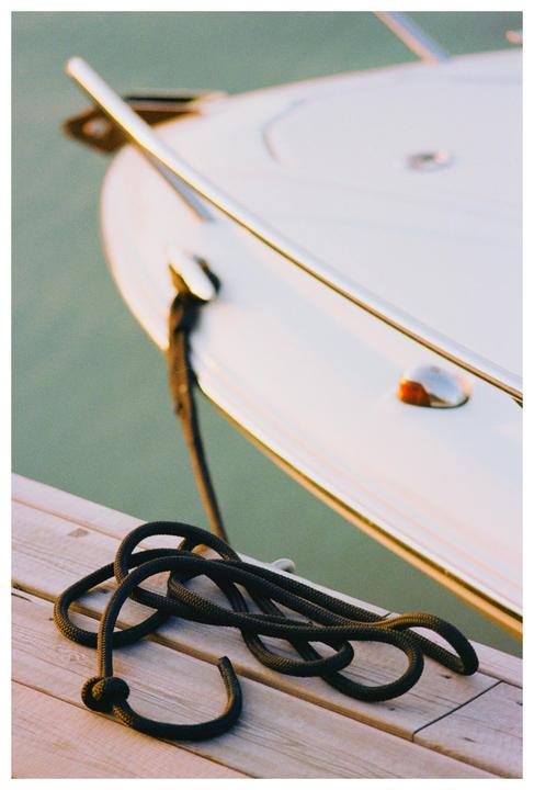 A black rope is coiled on a wooden dock next to a white boat.