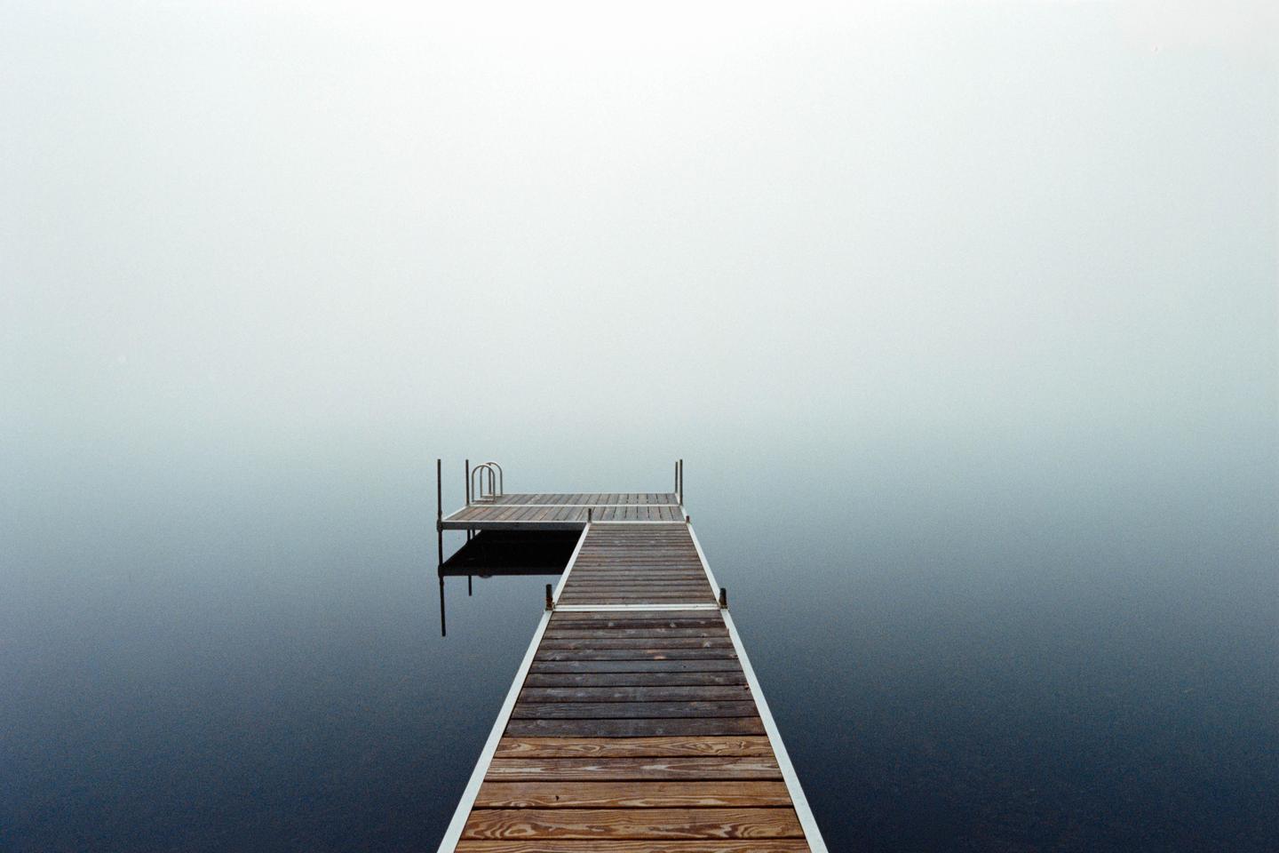 A wooden dock extends into a body of water shrouded in morning fog.