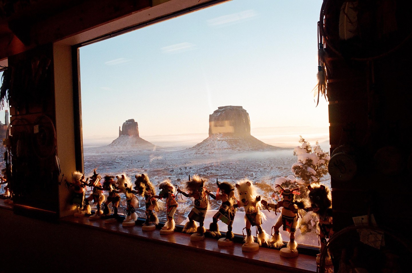 A row of figurines stands on a windowsill overlooking a snowy landscape with two large rock formations.