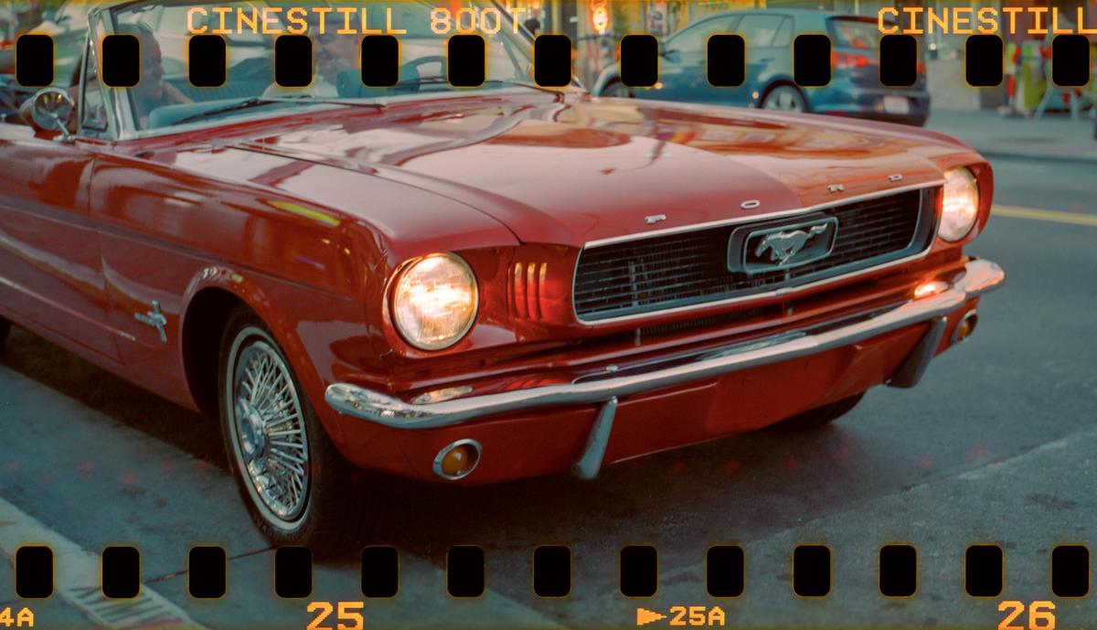 A red convertible car with its headlights on is parked on a street.