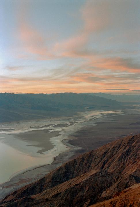 A vast desert landscape with mountains and a salt flat is visible under a sky with pink clouds at sunset.