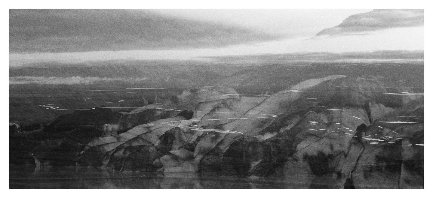A winding river flows through a mountainous landscape under a cloudy sky.