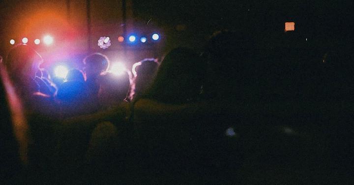 A crowd of people is visible in silhouette against bright stage lights at night.
