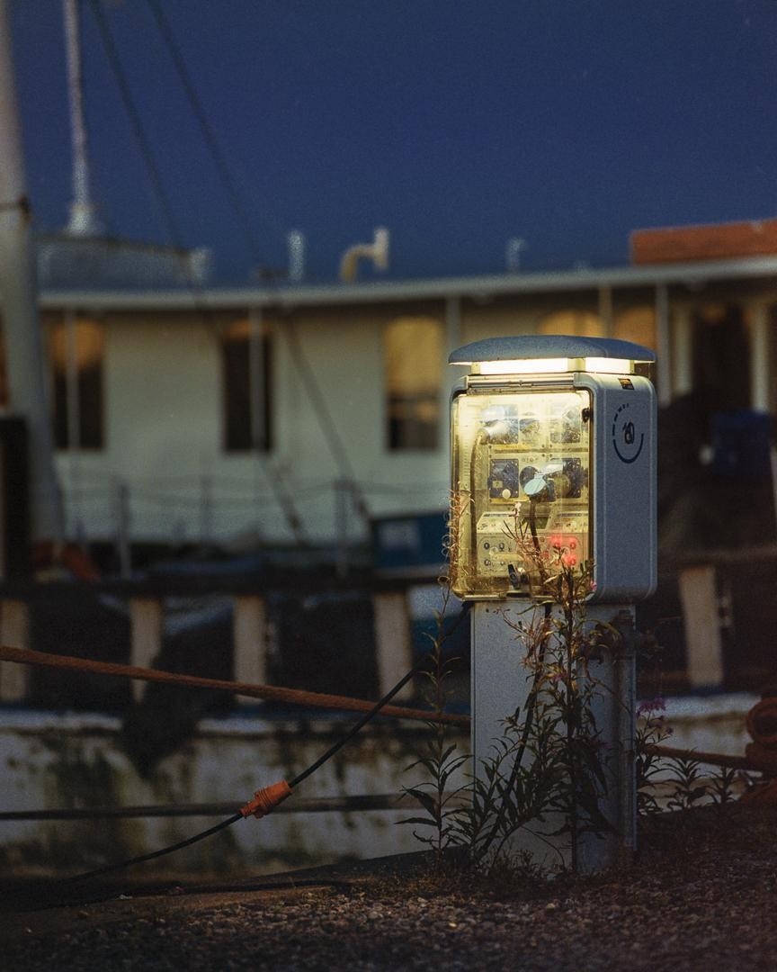 A ground power box with a glowing light stands in the foreground, with a boat and dark sky in the background.