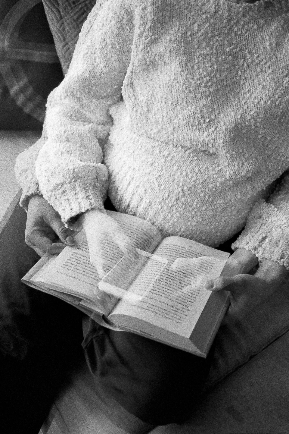 A person wearing a textured sweater holds an open book with both hands.