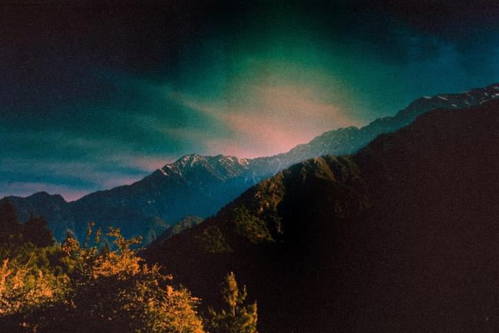 A mountain range with snow-capped peaks is visible under a colorful sky.