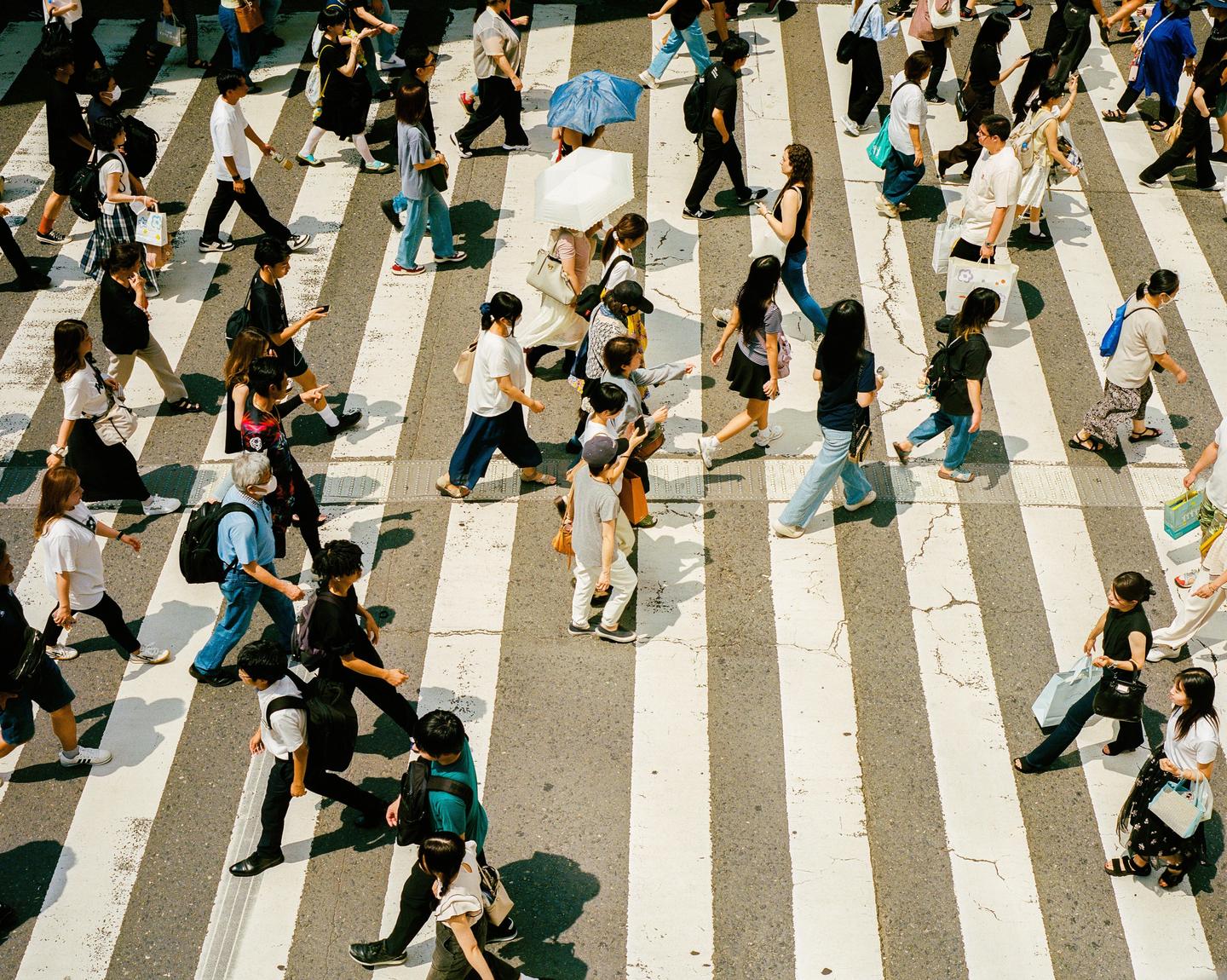 A large group of people are crossing a street on a crosswalk, with some carrying umbrellas.